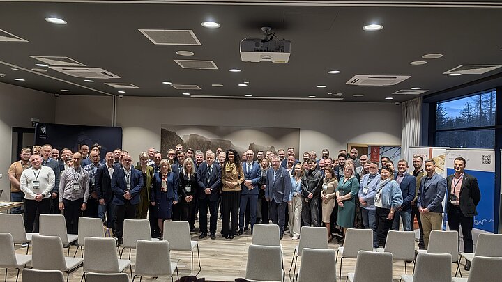 Na zdjęciu widać uczestników Zimowej Szkoły Gemoechaniki i Geotechniki. Uczestnicy ubrani w galowe stroje stoją obok siebie w nowoczesnej sali konferencyjnej.