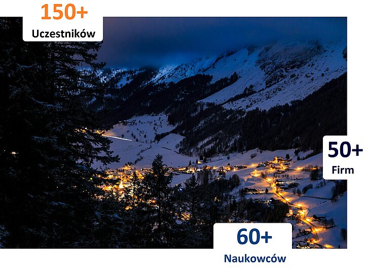 Na zdjęciu widać oświetlone miasteczko nocą. Miasteczko pokryte jest śniegiem. Z boku zdjęcia znajdują się napisy: ponad 150 uczestników, ponad 50 firm, ponad 60 naukowców.